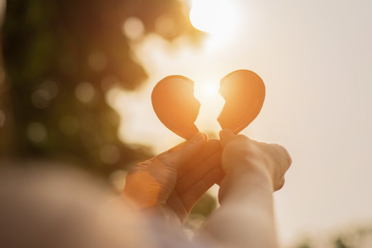 Silhouette broken heart,close up woman hand holding broken heart in the park.

