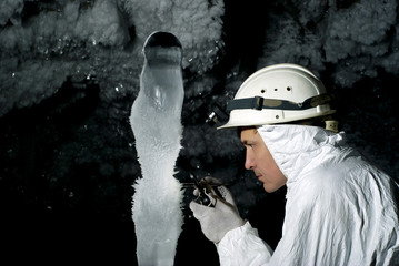 speleologist in a cave examines a giant ice stalagmite covered with hoarfrost, against a background...