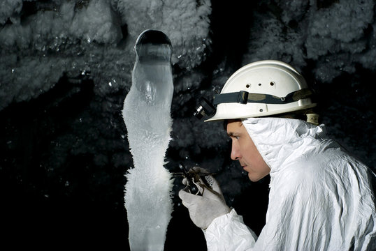 speleologist in a cave examines a giant ice stalagmite covered with hoarfrost, against a background of a dark rock covered with ice crystals