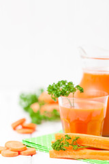 Carrot juice in beautiful glasses, cut orange vegetables and green parsley on white wooden background. Fresh orange drink. Close up photography. Selective focus. Vertical banner