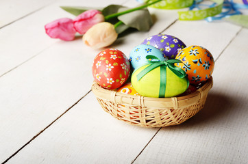 Rustic style painted easter eggs in basket on white table