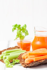 Carrot juice in beautiful glasses, cut carrot and green celery on wood bark bowl on white wooden background. Fresh vegetable drink. Close up photography. Selective focus. Horizontal banner