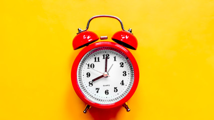 Red alarm clock on yellow background. Concept back to school. The hands of the clock are set to...