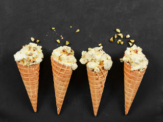 Four ice cream in waffle cone with nuts on black