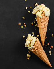 Two vanilla ice cream in waffle cone with nuts on black