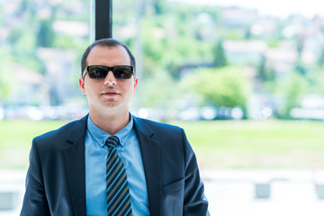 a portrait of a business man with a sun-glasses in his office. Confident business man, ceo, owner in his modern office in front of window.