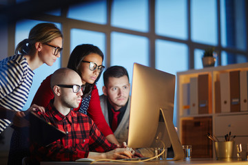 Young serious designers reading online data or watching videos about new trends while working late in the evening