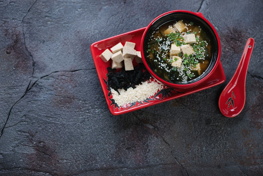 Red tableware with miso soup on a gray cracked asphalt background, above view with space, horizontal shot