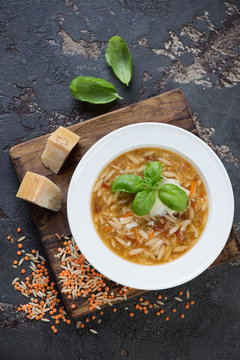 Plate of italian soup with lentils and pasta on a wooden serving board, view from above on a brown stone background