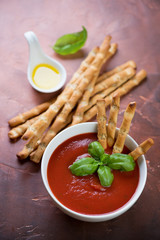 Cold tomato soup gazpacho with salted breadsticks and fresh basil, studio shot on a rusty metal surface, selective focus