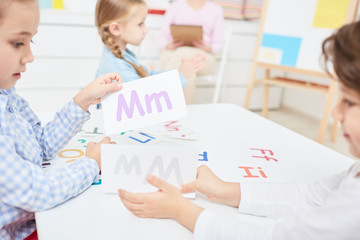 Two kids choosing paper cards with english letters during lesson in kindergarten or elementary school