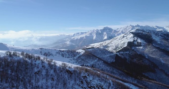 Forward aerial on white snow mountain peak in winter revealing valley.Forest woods.Snowy mountains establisher with backlit sun.Italian Alps.4k drone flight establishing shot