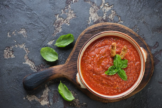Cold gazpacho tomato soup on a rustic wooden serving board, top view on a brown stone background, horizontal shot with space