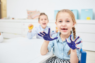 Funny little girl with blue painted palms looking at you while playing in kindergarten