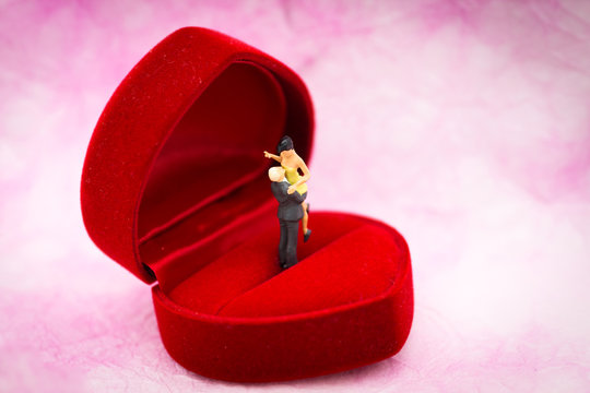 Miniature people: Couple hug each other to show love on wedding ring box. Image use for Valentine's day concept.