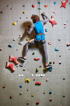 Contemporary young man in activewear practicing wall climbing in gym