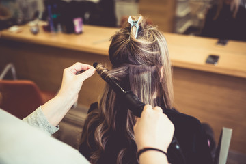 Hairstylist making curls to woman client in hairdressing beauty salon. 