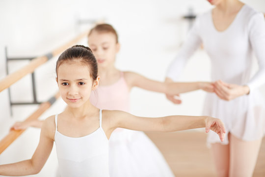 Attractive little ballerinas training in classroom with their teacher help