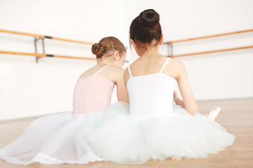 Fototapeta premium Rear view of little ballerinas having rest on the floor between classes of dancing