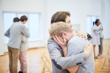 Young man supporting his crying friend in need during psychological course