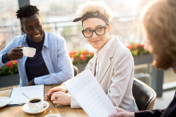 Young designer or manager listening to one of male colleagues during working conversation at meeting in cafe