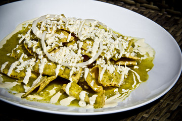 Green Chilaquiles with fresh crumbled cheese and sour cream, hard light close-up.	