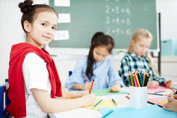 Diligent schoolgirl looking at camera while drawing with crayons and highlighters