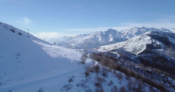 Side aerial on white snow mountain peak in winter revealing skier ski chair lift.Forest woods.Snowy mountains establisher with backlit sun.Italian Alps.4k drone flight establishing shot
