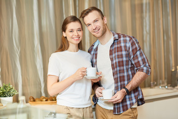 Smiling young couple spending time in the kitchen by cup of tea or coffee