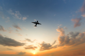 Silhouette of turboprop airplane flying in orange sky at sunset, wide angle, focus on plane, blurred clouds, copy space/ View of a flying airplane from below/ Vacation, aviation, trip concept
