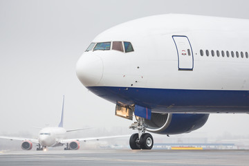 Fototapeta na wymiar Bad weather, aviation, transportation, travel concept/ Close up of wide-body airplane taxing on runway and preparing to take off, low-cloud conditions, poor visibility, foggy weather in cold season