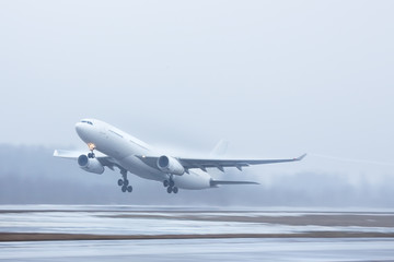 Bad weather, aviation, transportation,  travel concept/ Wide-body airplane take off in low-cloud conditions, poor visibility and foggy weather in cold season, copy space, horizontal, in motion/ 
