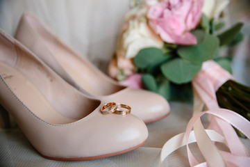 Wedding rings, beige sandals, a bouquet of flowers and boutonniere at the window. Accessories for wedding. The symbols of love, wedding rings,shoes, wedding bouquet