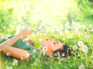 Obraz premium Piękna młoda kobieta, leżąc na zielonej trawie i dmuchanie mniszek lekarski. Koncepcja bez alergii