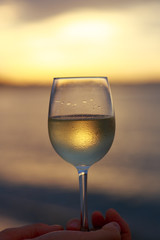 Wineglass of white wine at sunset dramatic sky background. Closeup. Travel vacations concept.
