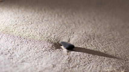 Single small stone lying on the beach, sandy abstract blurred background. Toned image with selective focus.