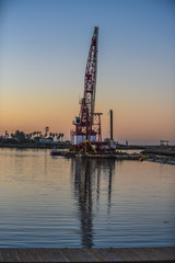 Obraz premium Long boom of marine crane extends into dawn sky as reflection in calm waters reaches toward the dock.