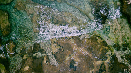 Aerial view of waves break on rocky beach. Sea waves on the beautiful colorful rocky beach. Aerial view drone 4k shot. Zoom in