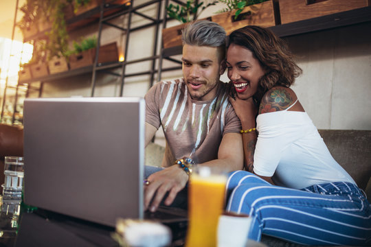 Young interracial lovers spending time in cafe watching media together on laptop