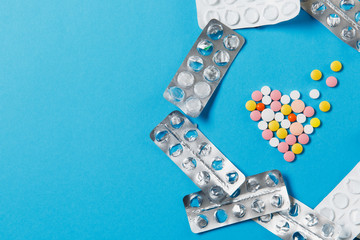 Medication colorful round tablets in form of diffusion heart isolated on blue background. Empty packings around Pills shape. Health treatment choice healthy lifestyle concept. Copy space advertisement