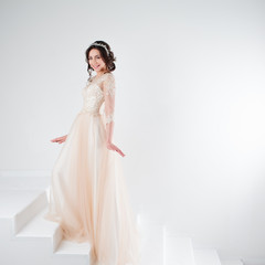 Fototapeta premium Portrait of a beautiful girl in a wedding dress. Bride in a luxurious dress standing on the stairs, climb up