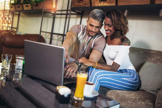 Young interracial lovers spending time in cafe watching media together on laptop