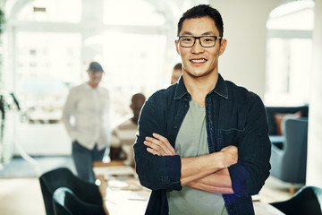 Smiling young Asian designer with colleagues working in the background