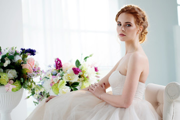 Portrait of a beautiful girl in a wedding dress. Bride in luxurious dress sitting on a chair