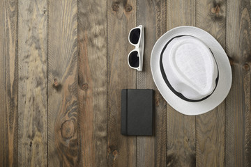 Sombrero blanco, gafas de sol y libreta sobre fondo de madera, vistos desde arriba