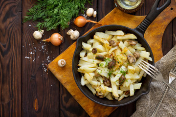 Fried potatoes with champignons mushrooms on the rustic kitchen table. Flat lay. Top view.