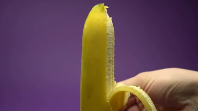 Peeling the skin from a banana. Violet background