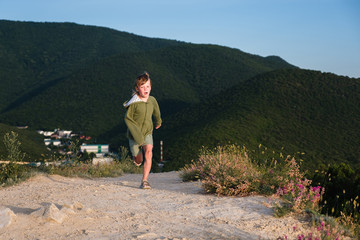 Fototapeta premium Six year old boy running on a mountain road at sunset with town view. Cool summer evening.