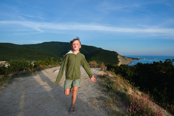 Naklejka premium Six year old boy running on a mountain road at sunset with town and sea view. Cool summer evening.