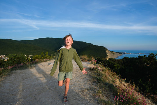 Six year old boy running on a mountain road at sunset with town and sea view. Cool summer evening.